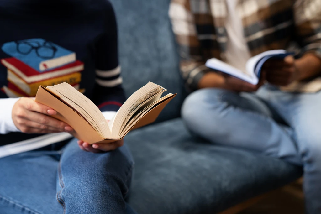 Zwei Personen sitzen nebeneinander und lesen in aufgeschlagenen Büchern