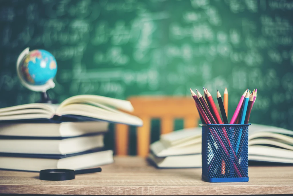 Aufgeschlagene Bücher, Buntstifte und ein Globus vor einer grünen Tafel